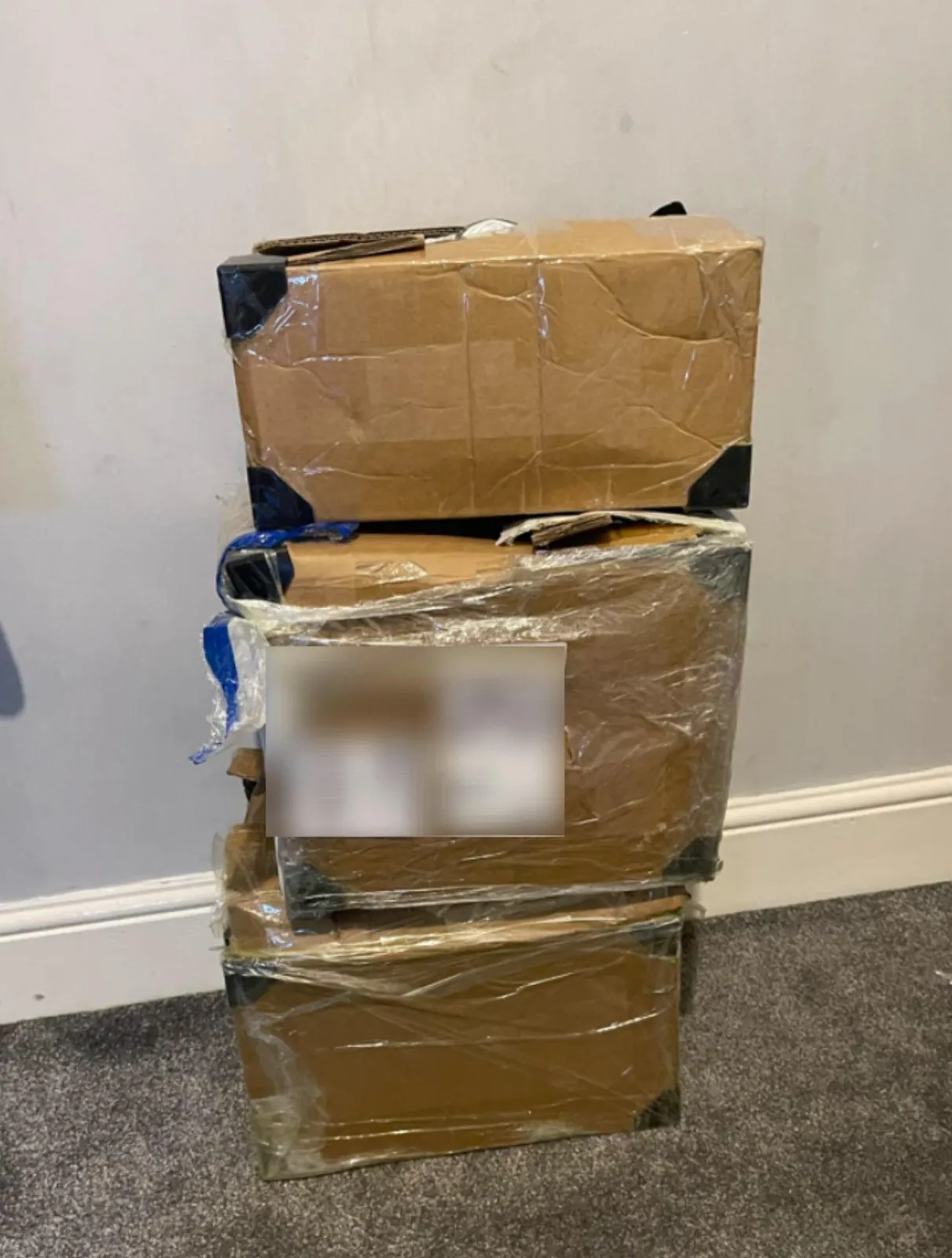 Three taped cardboard parcels stacked on carpet with the shipping label blurred