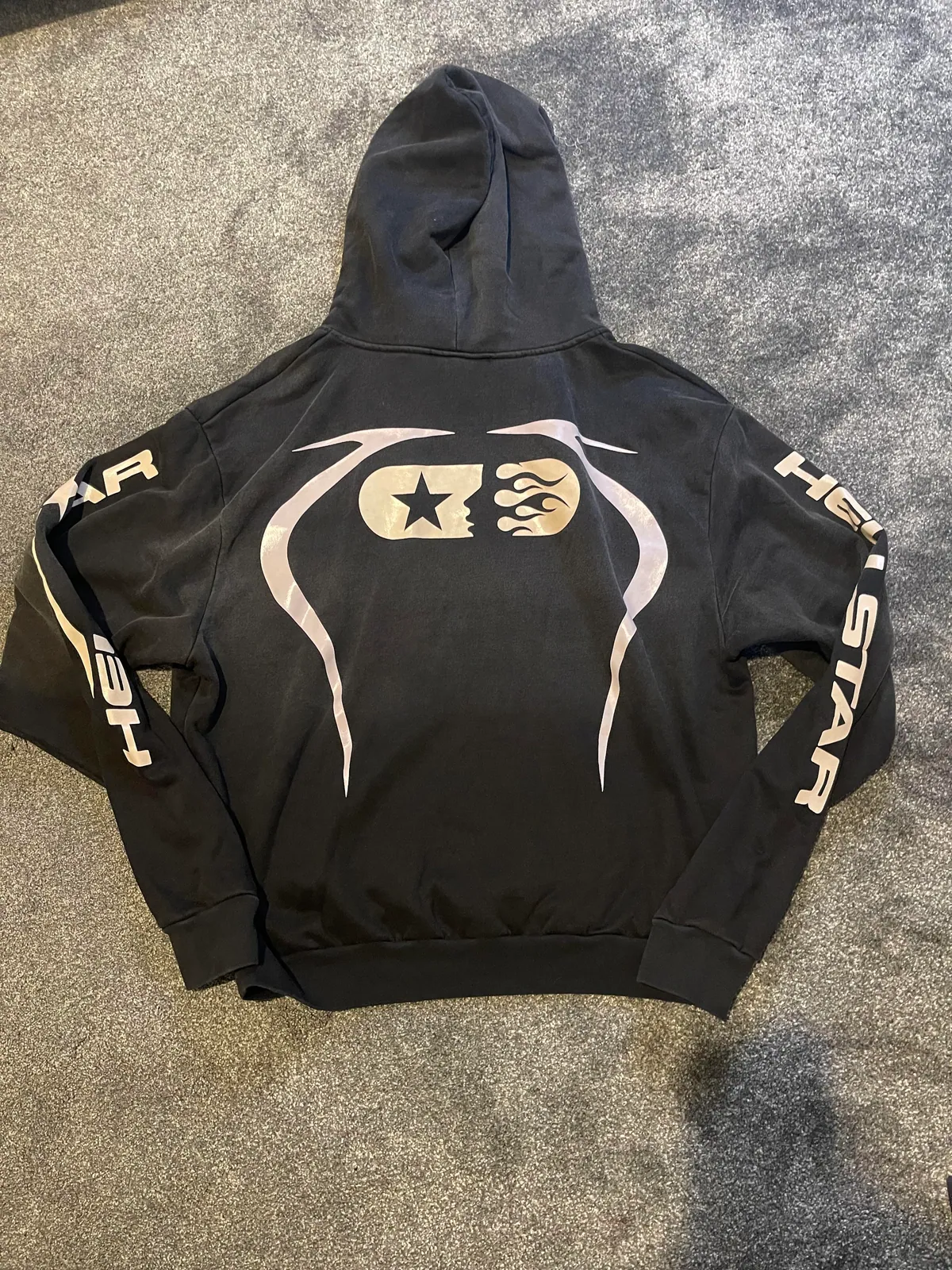 Back of a black hoodie with a large pale graphic and lettering on the sleeves