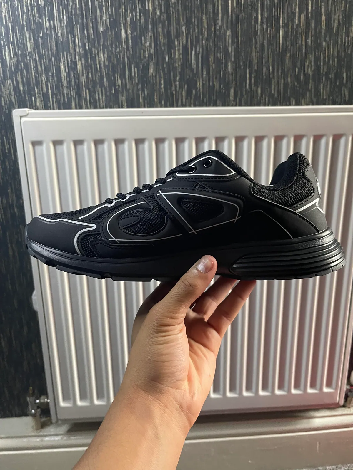 Black low-top sneaker with silver piping held in front of a radiator