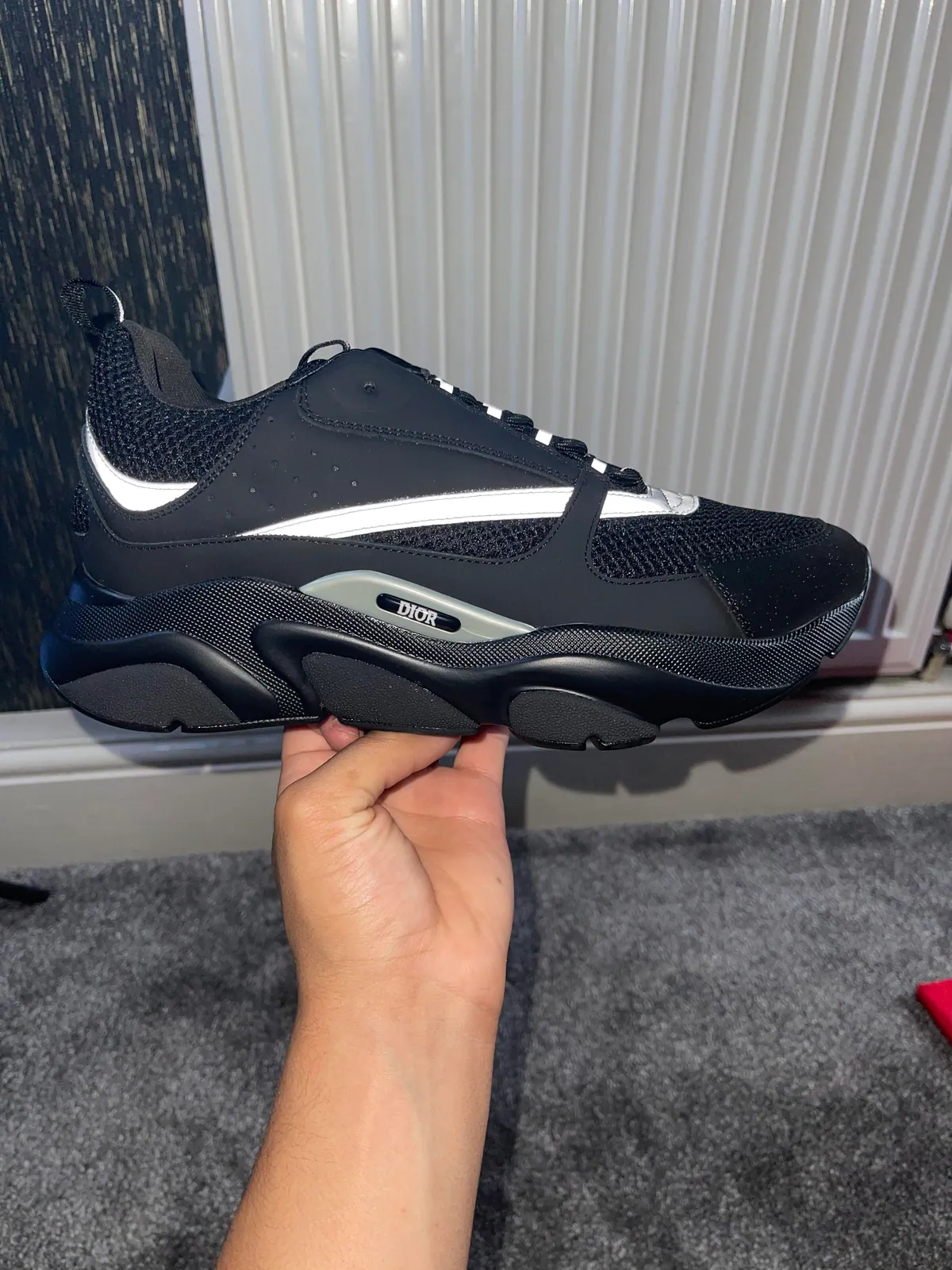 Black sneaker with reflective side stripes and a chunky sole held in one hand