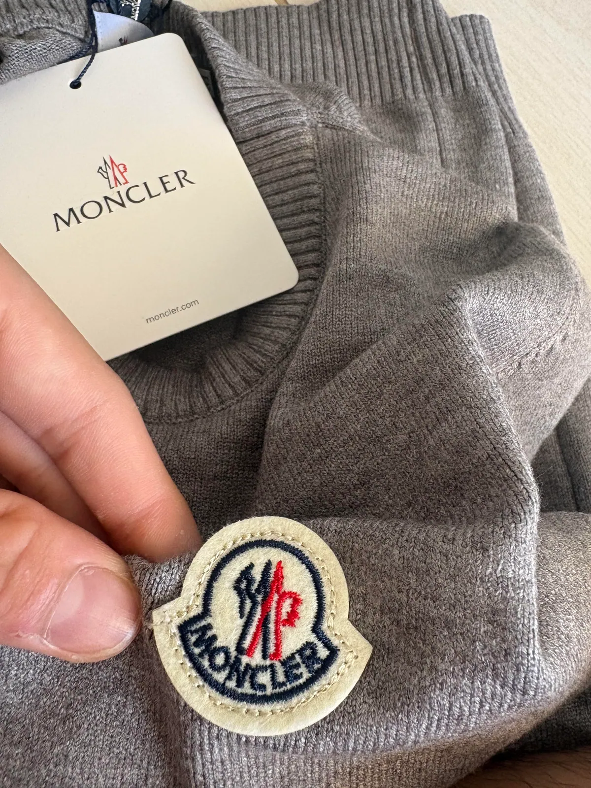 Circular badge and hanging tag on a gray knit sweater