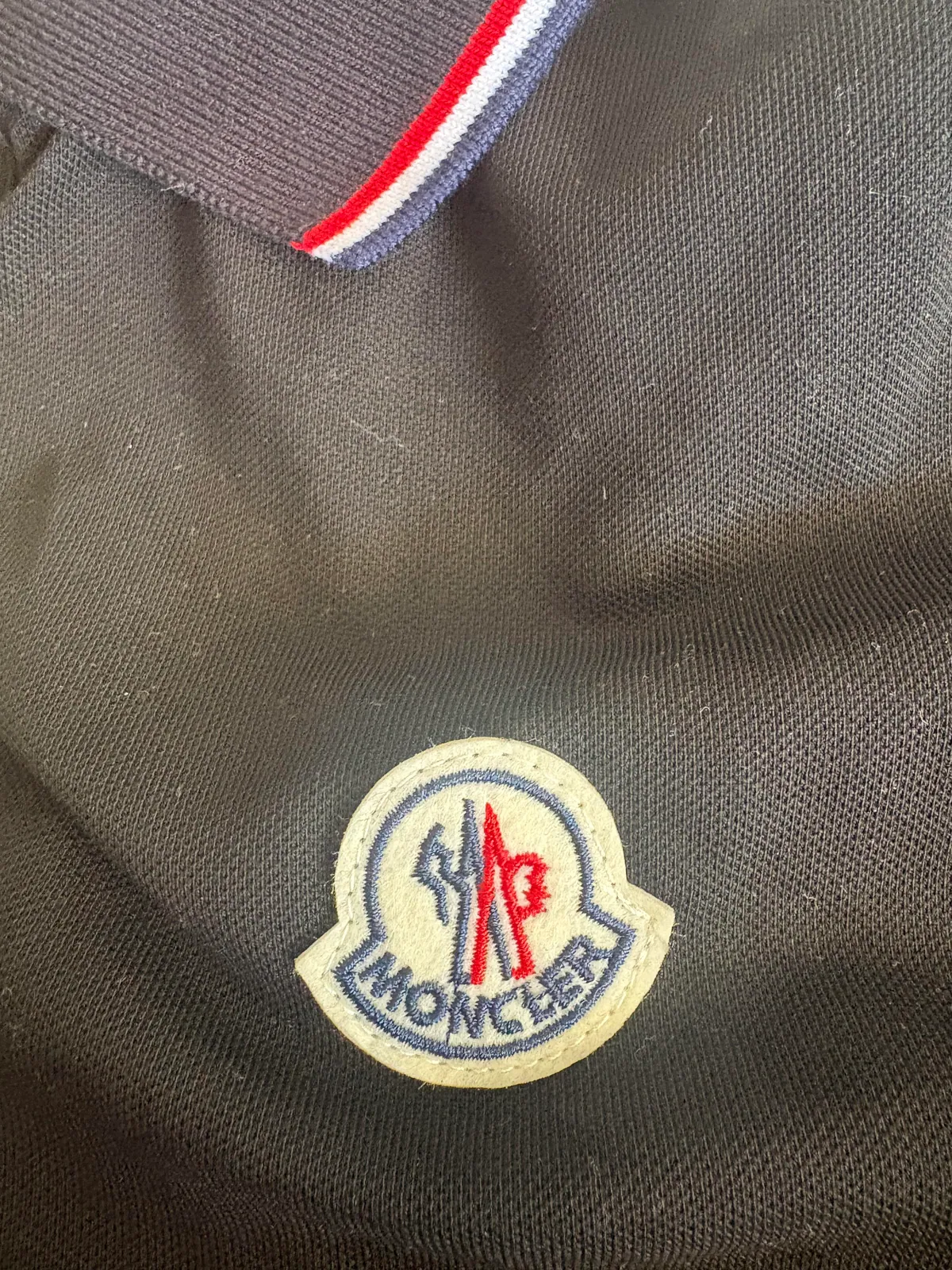 Circular chest badge and striped collar on a black polo shirt
