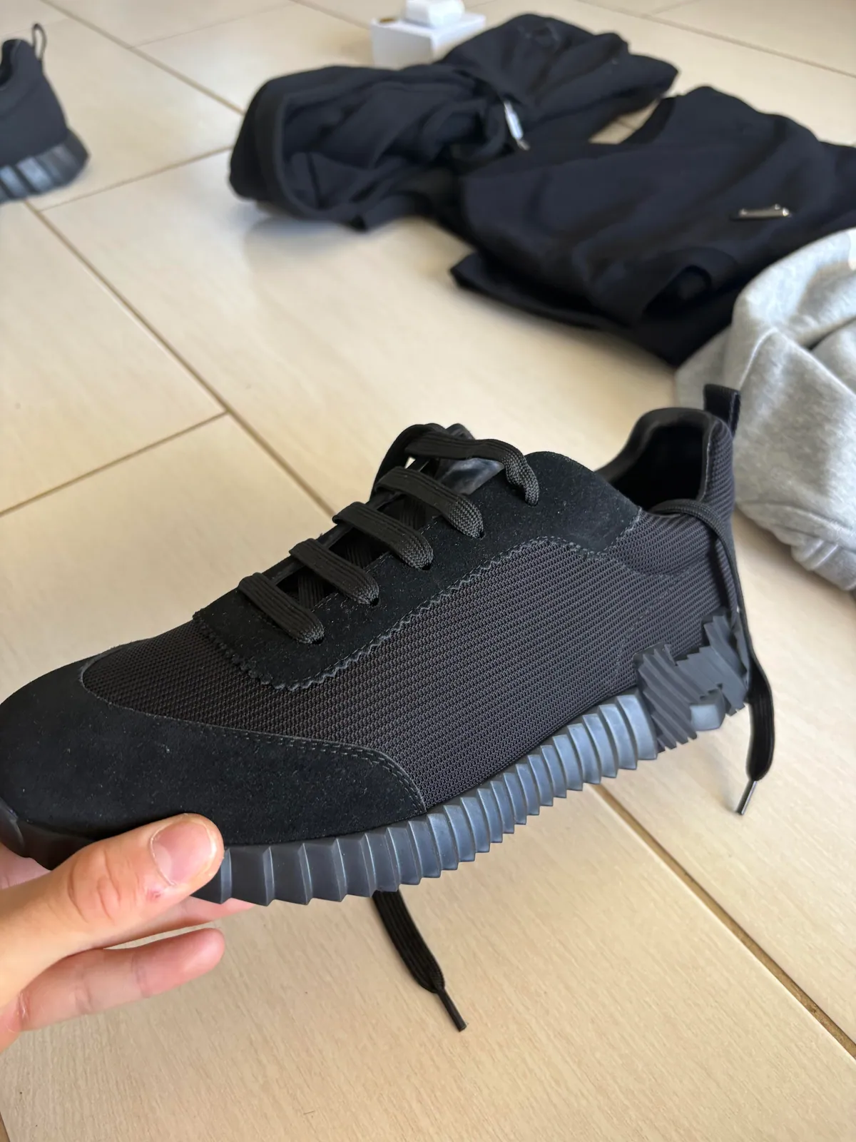 Black low-top shoe held to show the upper and gray outsole