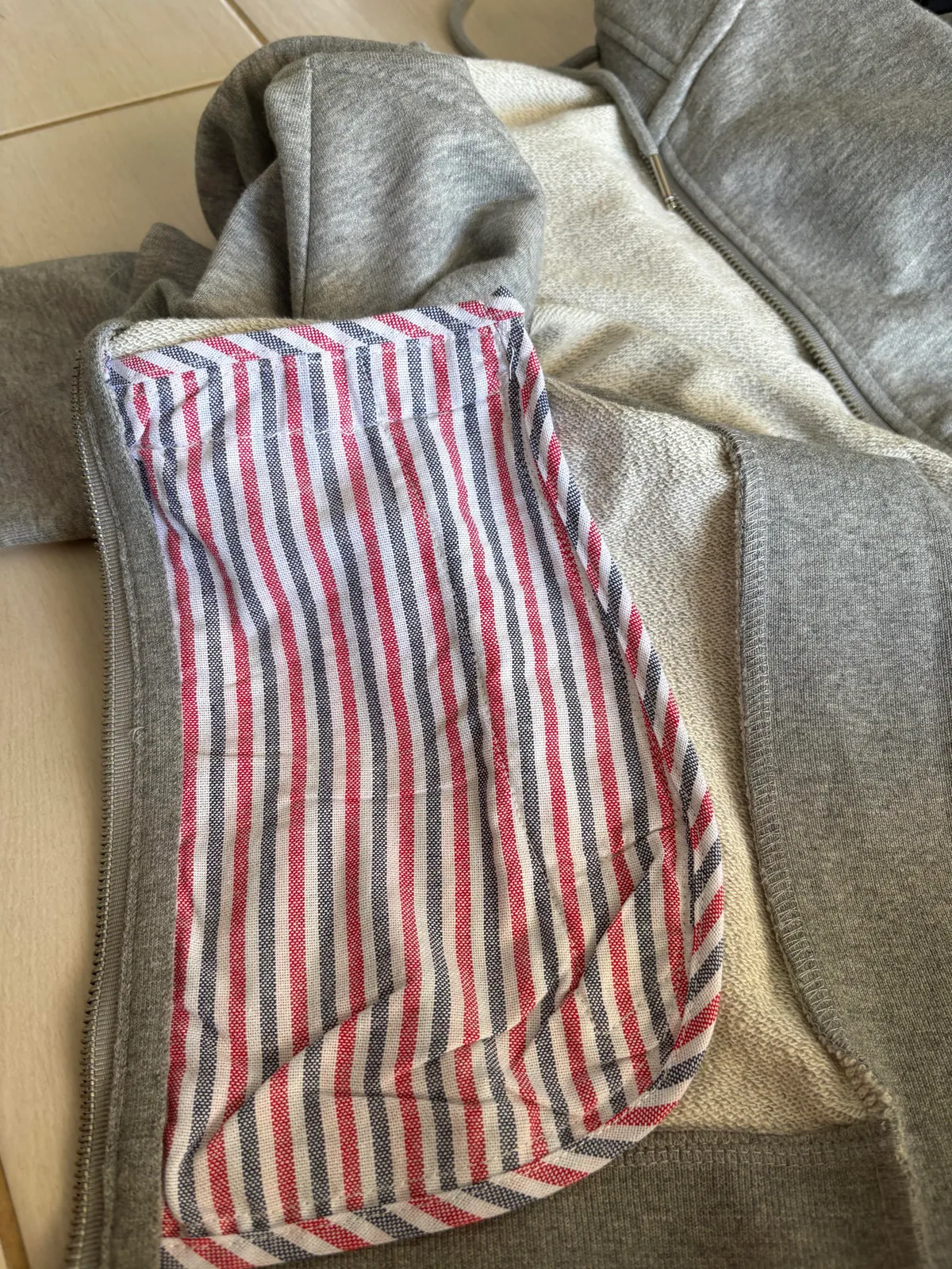 Inside of the gray zip-up garment showing looped fabric and striped trim