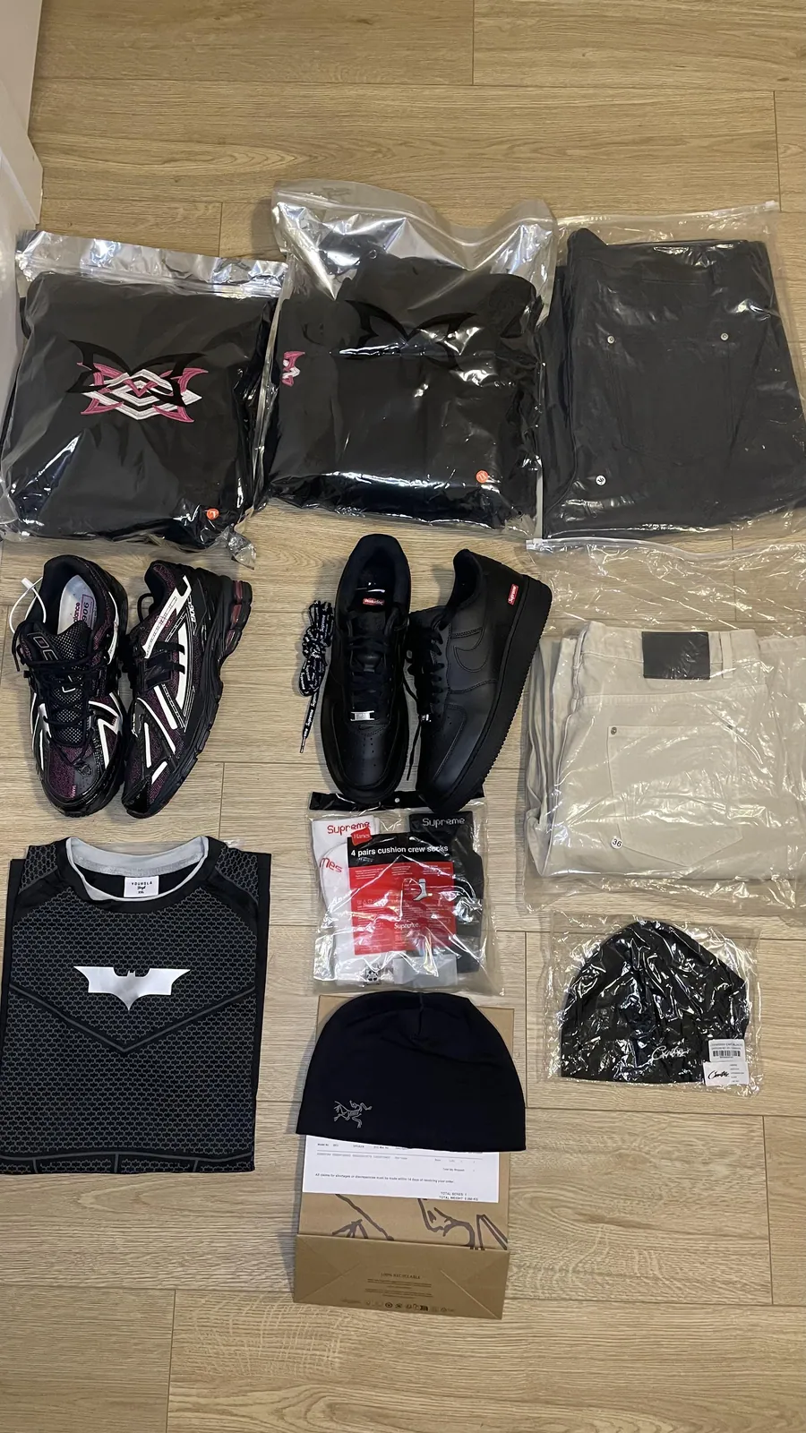 Flat lay of two shoe pairs, folded clothing, socks, denim and headwear on a wood floor
