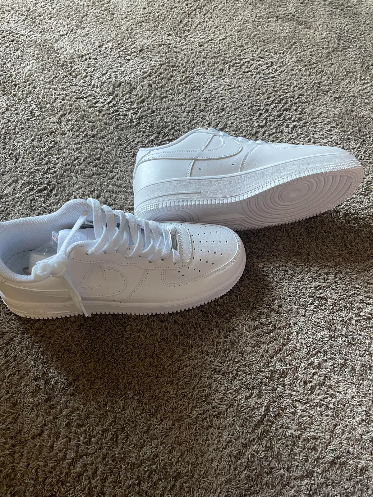 Two white sneakers shown from the side on carpet