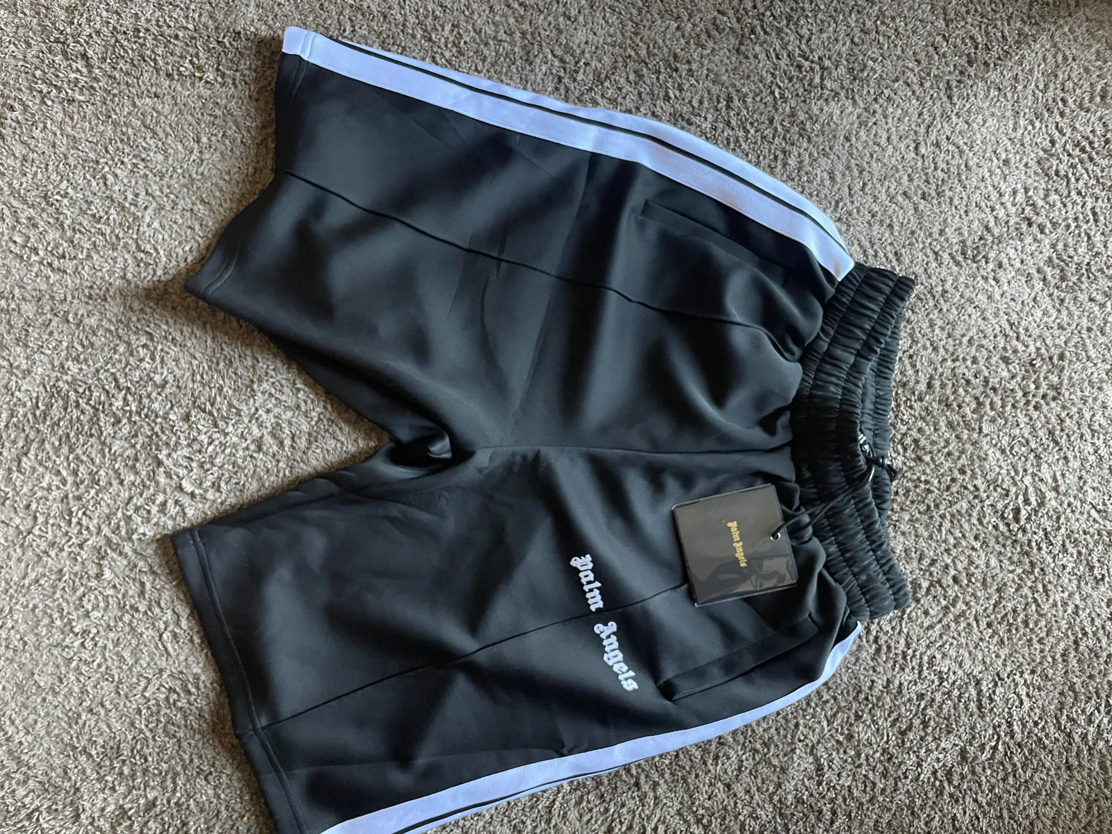 Black athletic shorts with pale side stripes laid flat