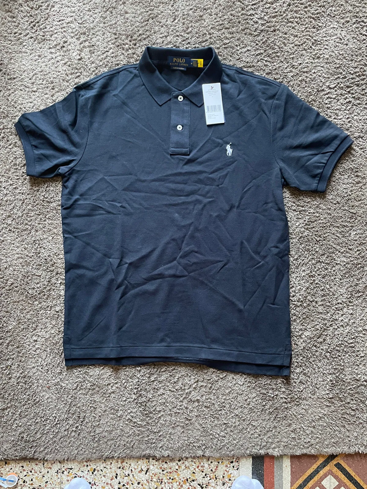 Navy polo shirt laid flat with its tag attached